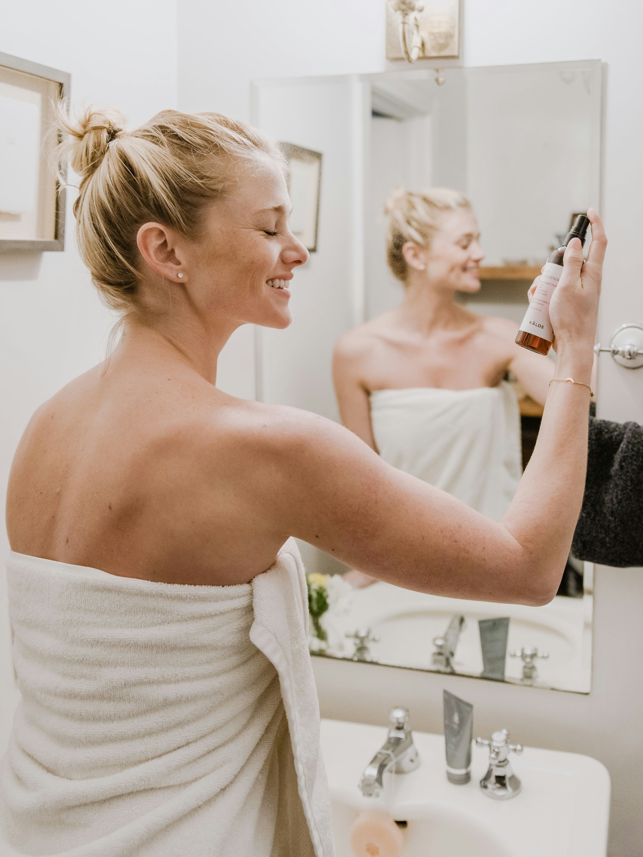 Woman smiling in mirror holding skincare product