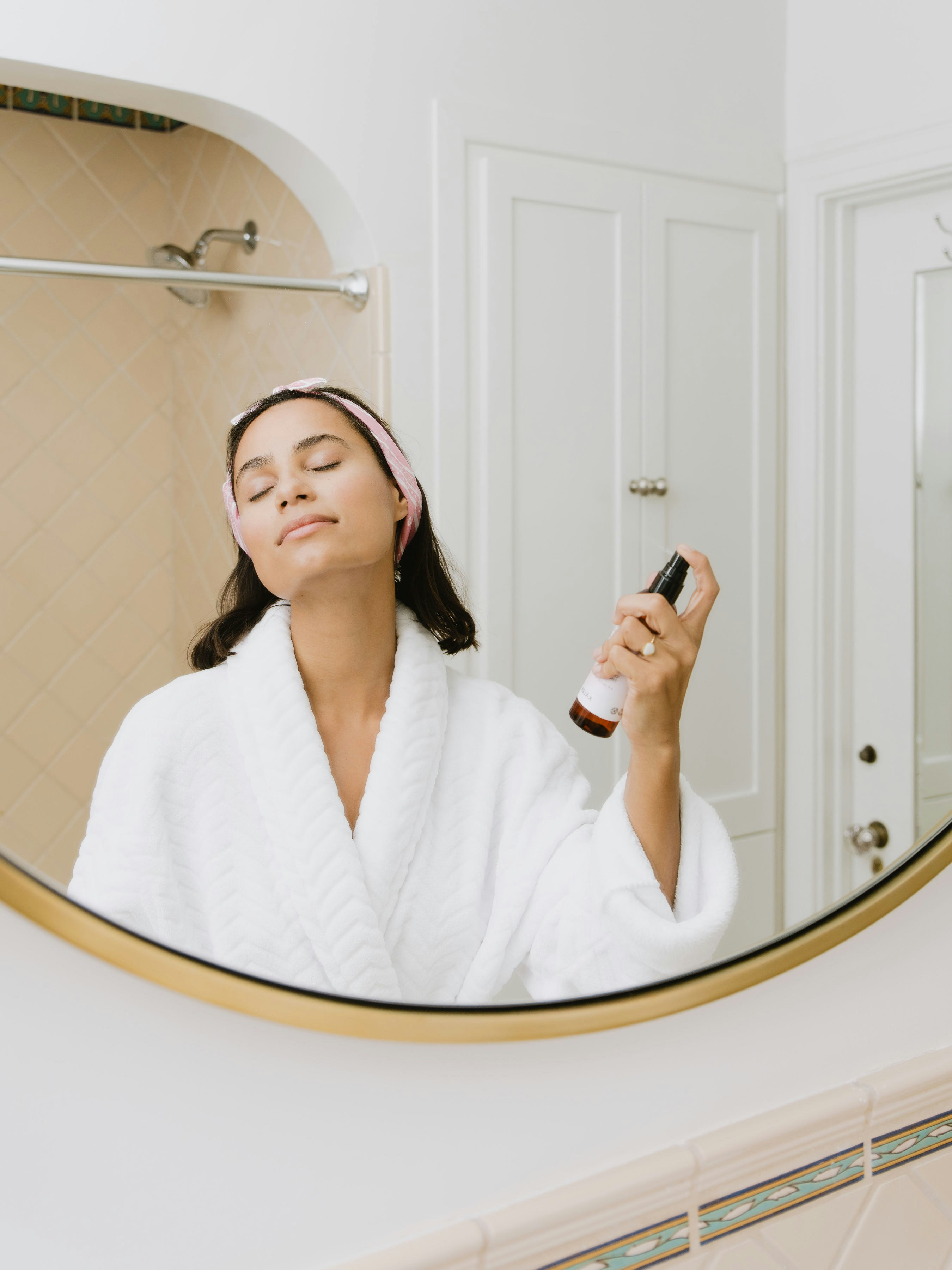 Woman in bathrobe with eyes closed applying skincare